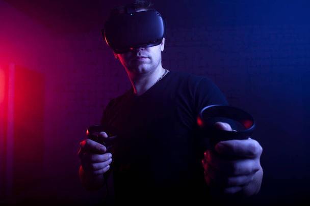 Kerl ein Gamer in drahtloser Brille der virtuellen Realität spielt einen Shooter, ein Mann konzentriert sich auf ein 3D-Spiel in einem dunklen Raum - Foto, Bild