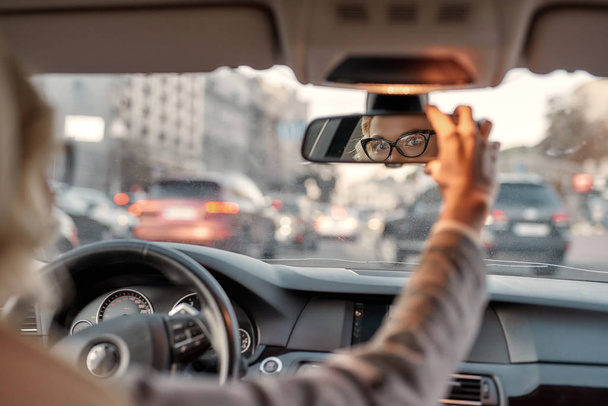 Conduz com cuidado. Mulher de negócios bonita sentada no banco da frente do carro e ajustando espelho retrovisor
 - Foto, Imagem
