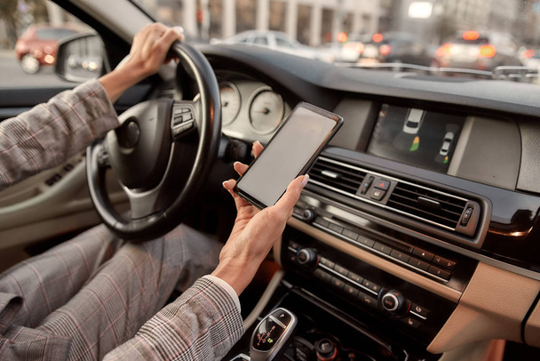 Käyttäen nykyaikaista teknologiaa. Rajattu kuva naisten käsi tilalla hänen älypuhelin ajon aikana auton
. - Valokuva, kuva