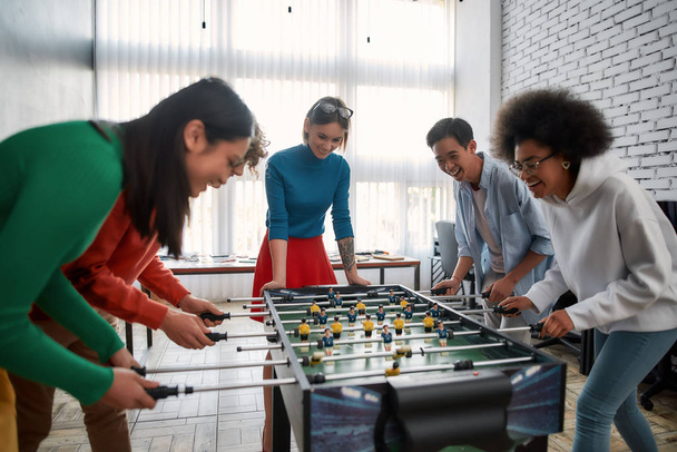 Happy team. Group of young and excited multicultural people in casual wear playing table soccer in the modern office and laughing. Office activities. Having fun together. Happy employees - Φωτογραφία, εικόνα