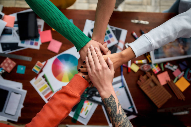 Building success together. Group of multicultural creative people stacking hands over the desk with graphic designers work tools and equipment on it. Web design concept. Teamwork - Photo, Image