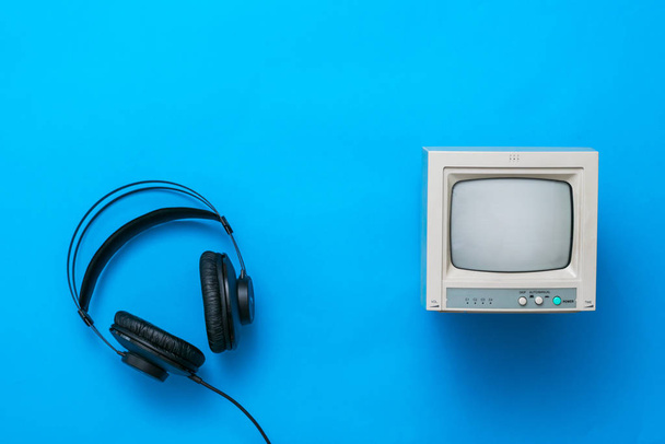 Black headphones with wire and a small retro monitor on a blue background. - Fotoğraf, Görsel