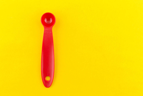 red measuring spoon of plastic on yellow background. - Fotografie, Obrázek