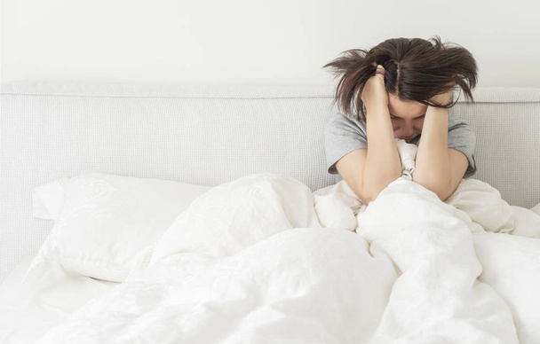 Upset sad young brunette woman sitting in bed at home, with copy space - Photo, Image