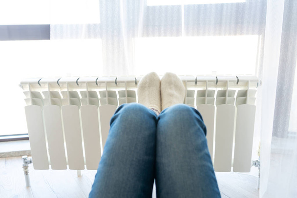 Woman warming up with feet on heater wearing woolen socks - Photo, Image
