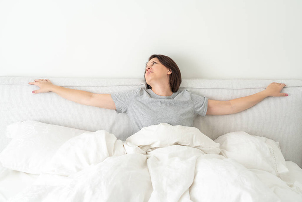 Улыбающаяся брюнетка в пижаме сидит в постели в спальне
 - Фото, изображение