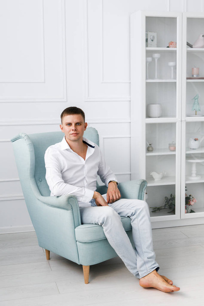 Handsome young man sitting in armchair indoors. Beautiful bright guest room - Valokuva, kuva