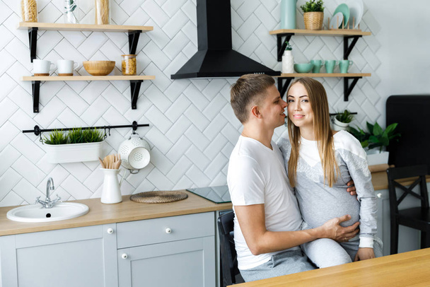 Młoda para - mężczyzna i kobieta spodziewający się dziecka, spędzają czas w kuchni. W oczekiwaniu na narodziny dziecka - Zdjęcie, obraz