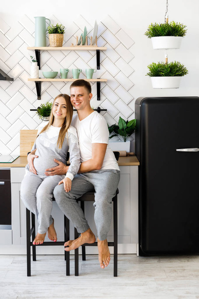 Young couple - man and woman expecting a baby, spend time in the kitchen. Awaiting the birth of a baby - 写真・画像