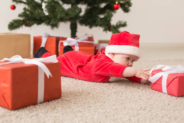 niedliches kleines Mädchen im Weihnachtsmann-Anzug, das auf dem Boden über den Weihnachtsbaum kriecht. Ferienzeit. - Foto, Bild