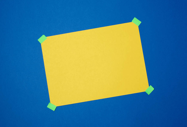 blank yellow sheet of paper stuck with green sticky tape on a bl - Photo, Image