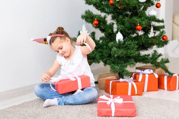 A srác karácsonyi ajándékokat nyit. Gyerek a karácsonyfa alatt ajándékdobozokkal. - Fotó, kép