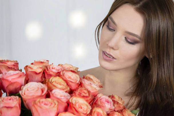 Beautiful face of the model and with a bouquet of roses. Woman with flowers. - Photo, Image
