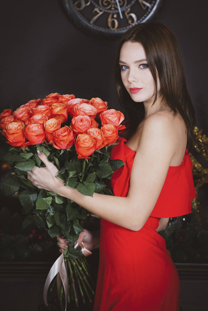 Beautiful girl in a red dress with a bouquet. Vertical. Model woman with roses. - Photo, image