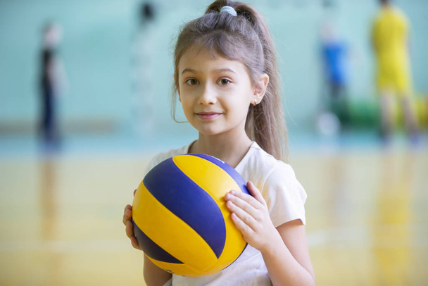 Child in the gym. Schoolgirl with a ball in a physical education lesson. Girl in a sports uniform. Children's training. Sports Day. - Valokuva, kuva
