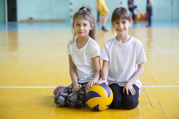 Dos colegialas con una pelota en el gimnasio. Retrato de un niño atleta. Lección de educación física
. - Foto, Imagen