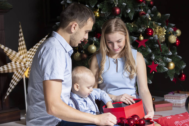 Familia en Navidad. Mamá papá e hijo en el árbol de Navidad
 - Foto, Imagen