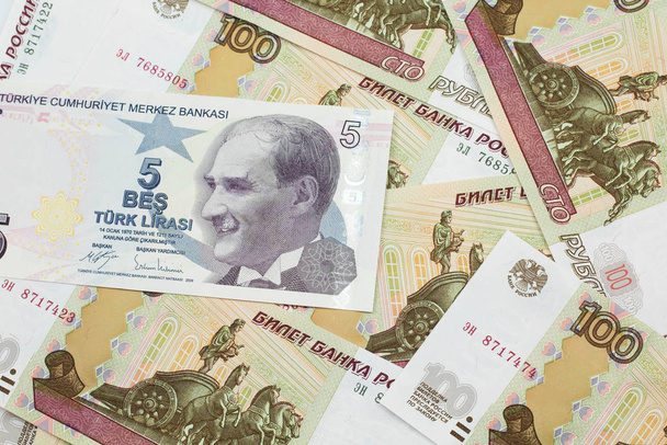 Κοντινή εικόνα πορφυρό χαρτονόμισμα πέντε τουρκικών λιρών σε φόντο ρωσικών εκατοντάδων ρουβλίων τραπεζογραμματίων σε μακροοικονομική βάση - Φωτογραφία, εικόνα