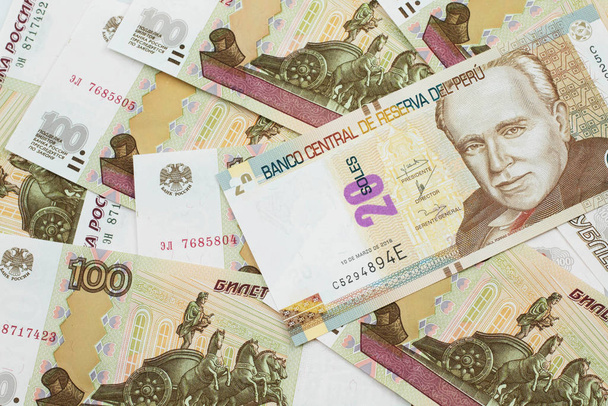 Une image en gros plan d'un nouveau billet de banque péruvien de vingt sols près sur un lit de billets de banque russes de cent roubles en macro
 - Photo, image