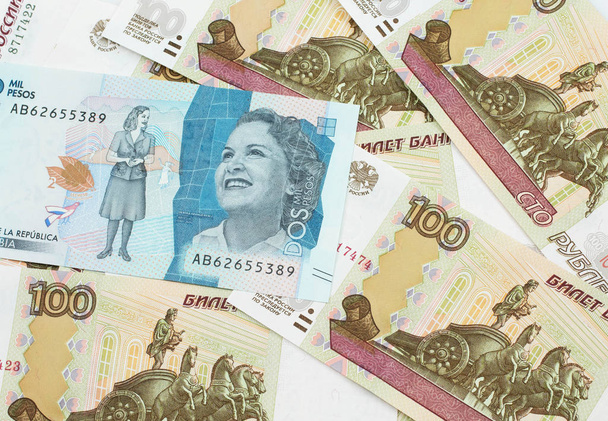 Detailní záběr modré dvou tisíc kolumbijských peso bankovek na pozadí ruských sto rublů bankovek v makru - Fotografie, Obrázek
