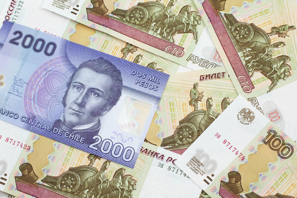 Una imagen de cerca de un billete púrpura de dos mil pesos de Chile en una cama de billetes rusos de cien rublos en macro
 - Foto, Imagen