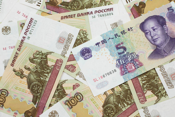 Un billete púrpura de cinco yuanes chinos se cierra en macro con billetes rusos de cien rublos
 - Foto, Imagen