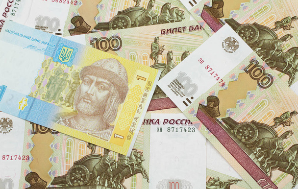 Een blauw en gele Oekraïense hryvnia bankbiljet op een bed van Russische honderd roebel bankbiljetten - Foto, afbeelding