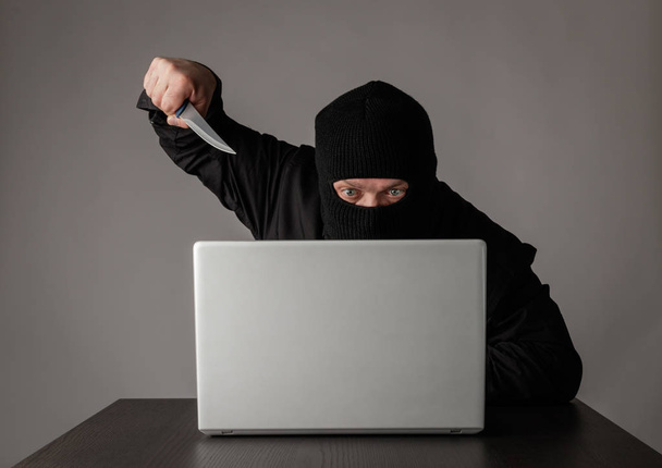 Hacker σε μάσκα χρησιμοποιώντας ένα φορητό υπολογιστή. - Φωτογραφία, εικόνα
