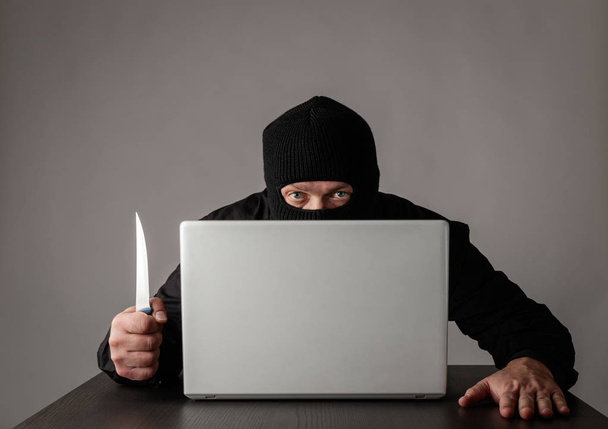 Hacker in mask using a laptop. - Foto, afbeelding