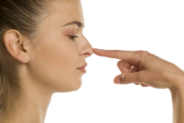 προφίλ της νεαρής γυναίκας αγγίζει τη μύτη της σε λευκό φόντο - Φωτογραφία, εικόνα