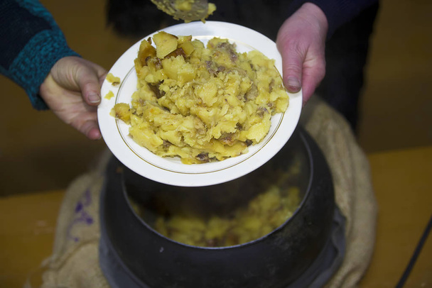 Rustieke aardappelstoofpot met gietijzer. Handen die voedsel vasthouden uit een Russische oven - Foto, afbeelding