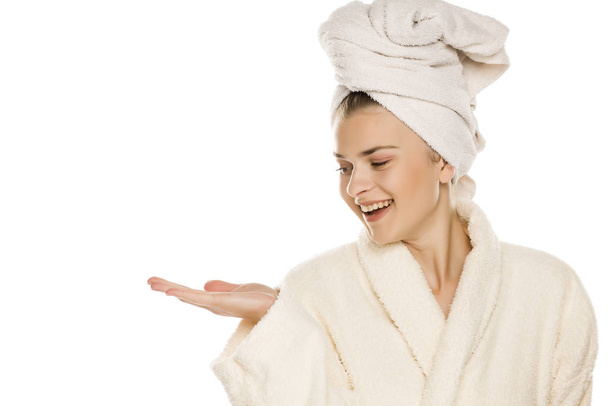 Young beautiful woman with towel on her head holding imaginary object on her hand on white background - Foto, afbeelding