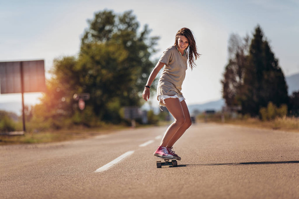 Młoda sportowa kobieta jeżdżąca na deskorolce po drodze. - Zdjęcie, obraz