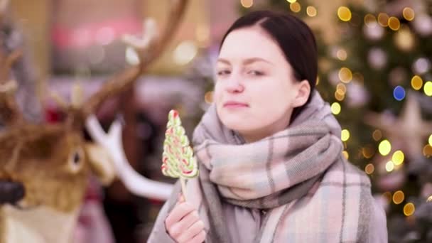 Een jonge vrouw die aan een lolly zuigt. Vrolijk meisje in kerstmis weekend veel plezier met snoep in haar handen. Kus snoep. Buiten, levensstijl. - Video