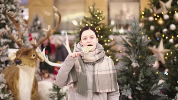 Een jonge vrouw die aan een lolly zuigt. Vrolijk meisje in kerstmis weekend veel plezier met snoep in haar handen. Kus snoep. Buiten, levensstijl. - Video