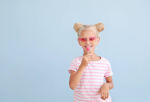 Cute little girl with lollipop on color background - Фото, изображение