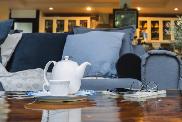 Fehér teáskanna csészével és szemüveggel mobiltelefonnal a fa asztalon otthon. - Fotó, kép