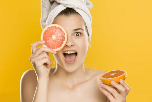 Portrait of young shirtles beautiful woman posing with grapefruit on yellow background - 写真・画像