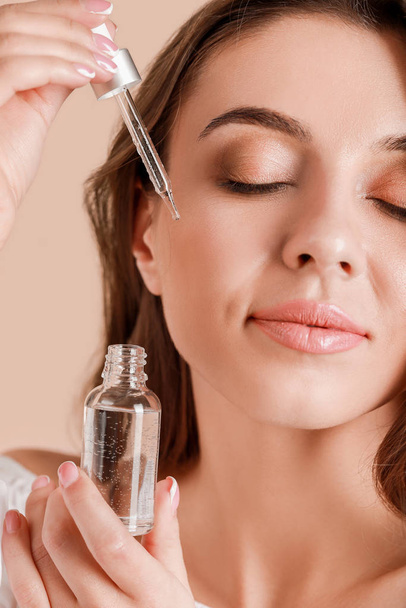 Beautiful young woman applying serum onto her skin against light background, closeup - Foto, Imagem