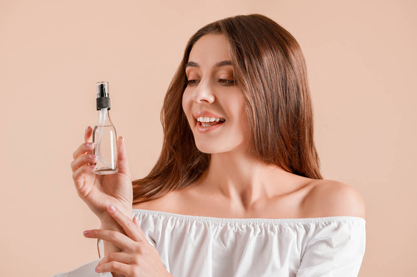 Beautiful young woman with bottle of cosmetics on light background - Φωτογραφία, εικόνα