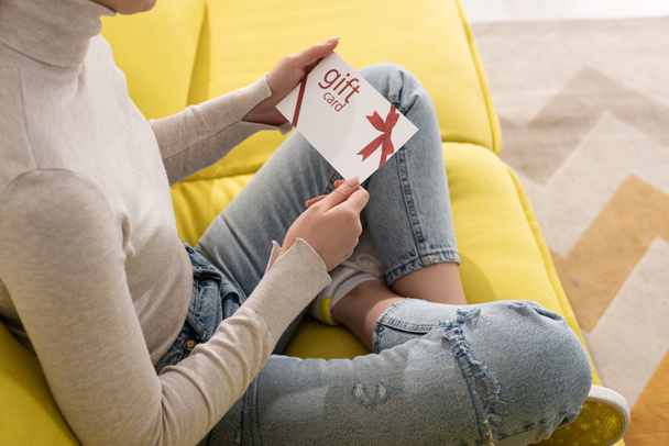 Cropped view of young woman holding gift card on sofa  - Фото, изображение