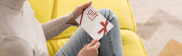 Vista cortada de jovem segurando cartão de presente no sofá, tiro panorâmico
 - Foto, Imagem
