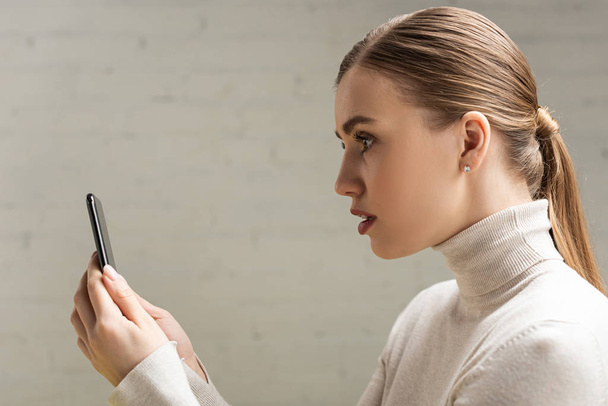 Vista lateral de mujer atractiva sosteniendo teléfono inteligente
 - Foto, imagen