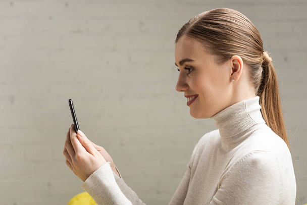 Side view of beautiful smiling girl holding smartphone - Foto, Imagen