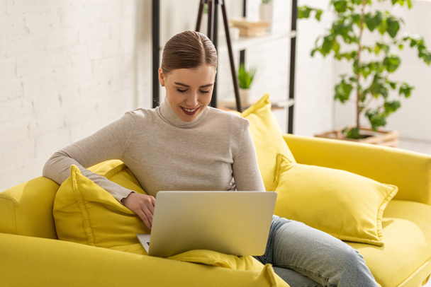 Hermoso freelancer sonriente usando el ordenador portátil en el sofá en casa
 - Foto, imagen