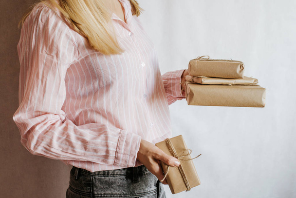 Woman holding many gift boxes in hand. Holiday present. Boxes with surprise. Happy celebration event. Kraft paper packaging. Wrapping paper and ribbon. Female hand with boxes close-up. Congratulation - Zdjęcie, obraz