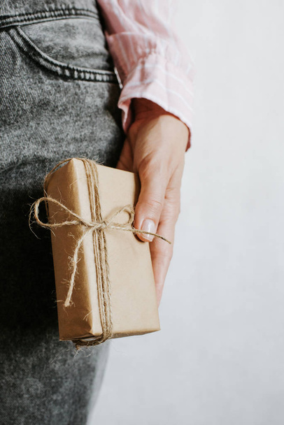 Woman hold gift in hand. Holiday present. Box with surprise. Happy celebration event. Kraft paper packaging. Wrapping paper and ribbon. Female hand with box close-up. Handmade congratulation - Fotoğraf, Görsel
