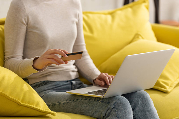 Cropped view of girl holding credit card and using laptop on sofa - Foto, Imagem
