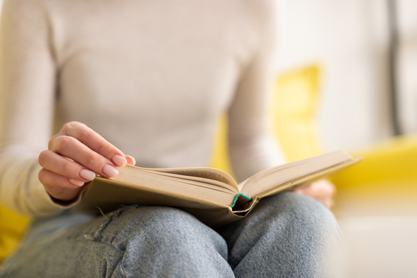 Cropped view of woman reading book on sofa at home - Photo, Image