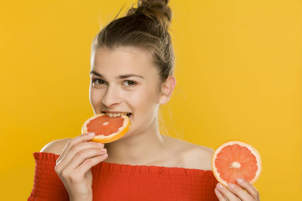 Young beautiful woman eating slices of grapefruit on yellow background - 写真・画像